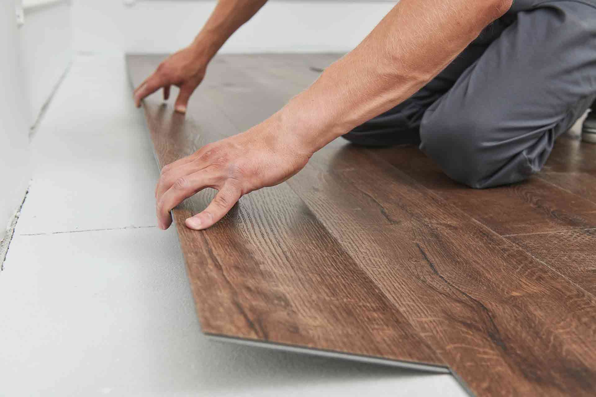 Kovi fitter laying dark-oak laminate planks on a prepped subfloor